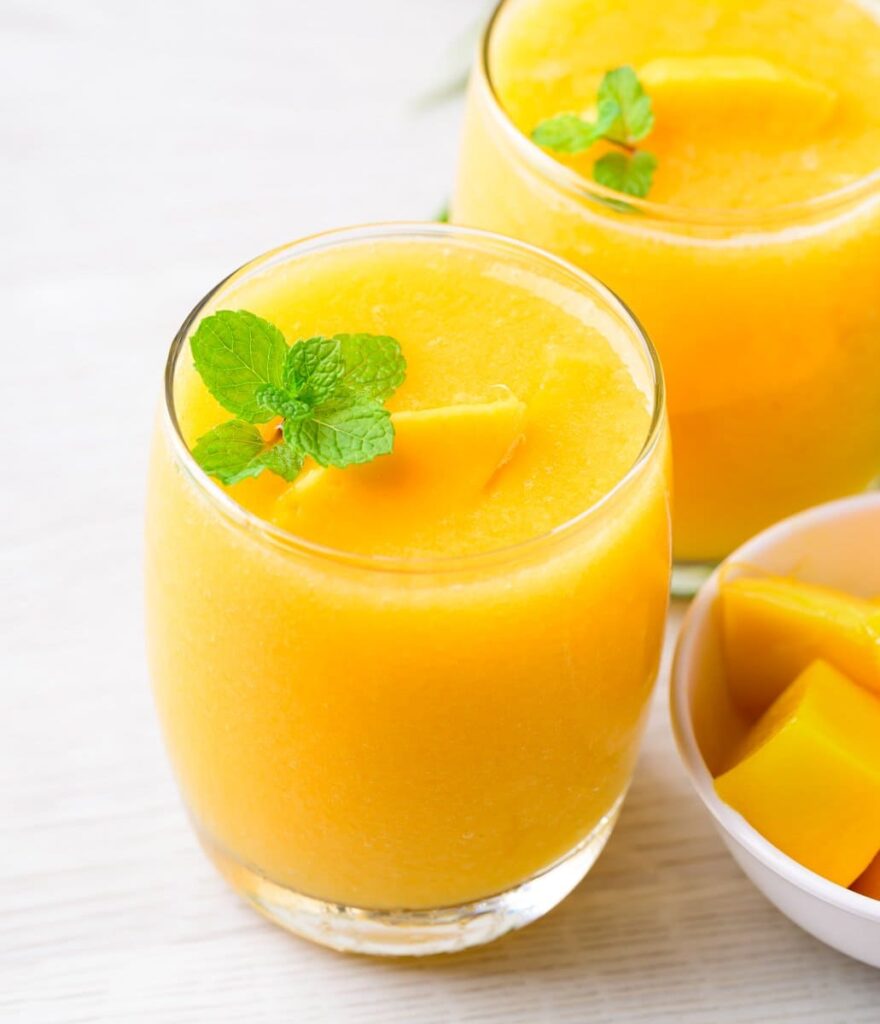 Overhead view of peach mango smoothie in a glass with fresh mangoes, peaches, and milk arranged around it on a marble background