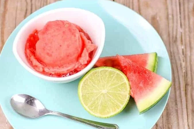 Vegan watermelon sorbet in a lime bowl garnished with fresh mint and lime zest on a white plate