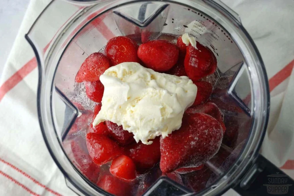 Blender filled with frozen strawberries and a scoop of vanilla ice cream ready to make Strawberry Dole Whip